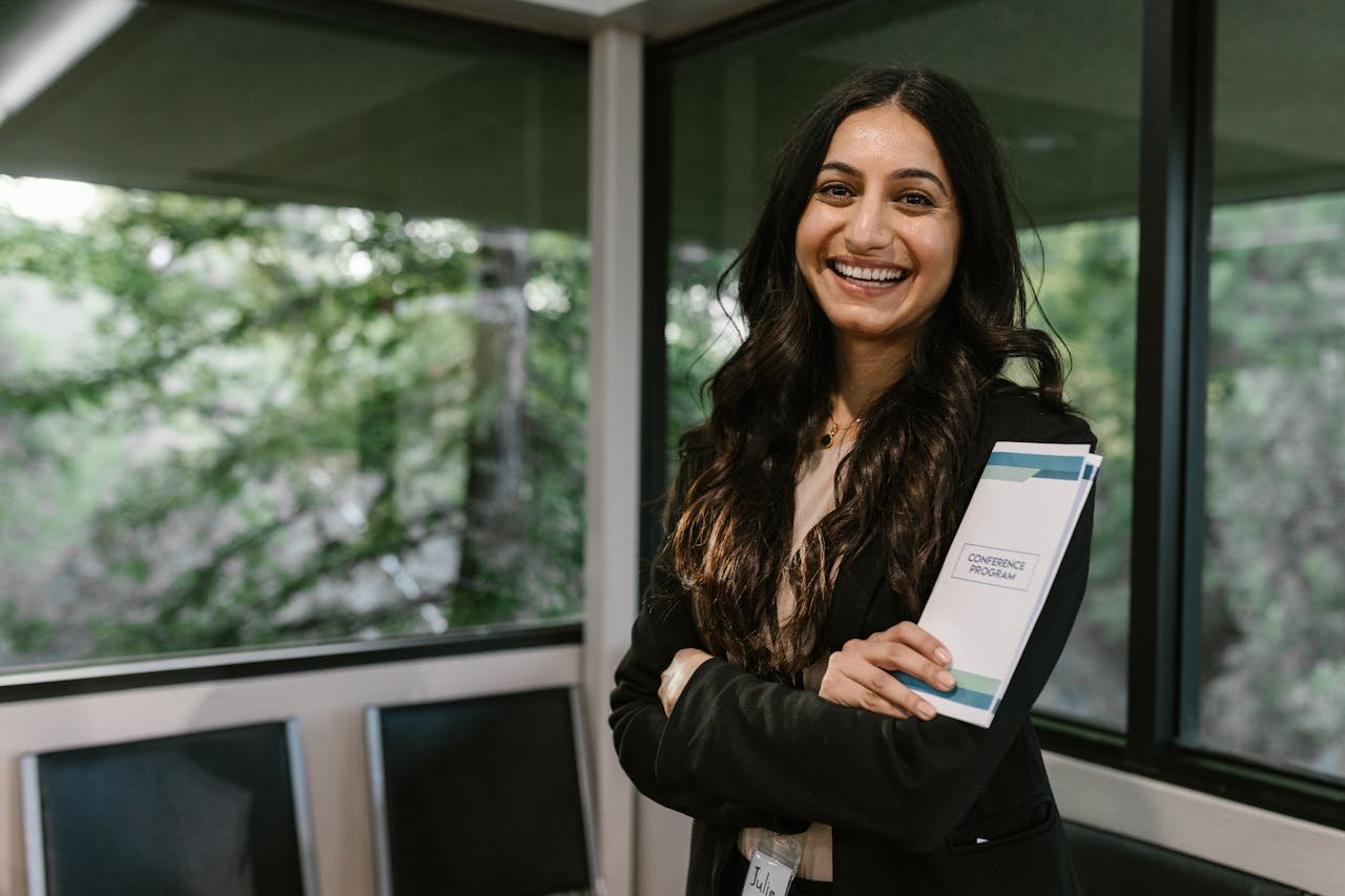 Confident woman holding conference program, smiling in modern indoor setting.